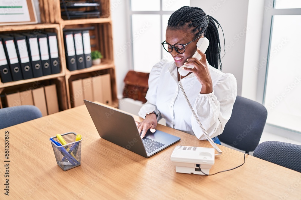 African american woman business worker talking on telephone using laptop at office African american woman business worker talking on telephone using laptop at office