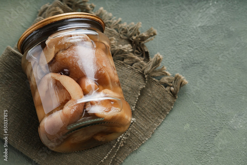 Glass jar with pickled forest mushrooms on a green napkin. Preserved mushrooms on a green background. Top view