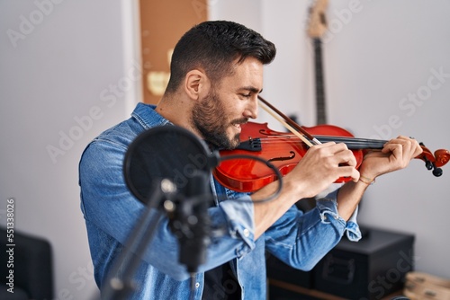 Young hispanic man musician playing violin at music studio