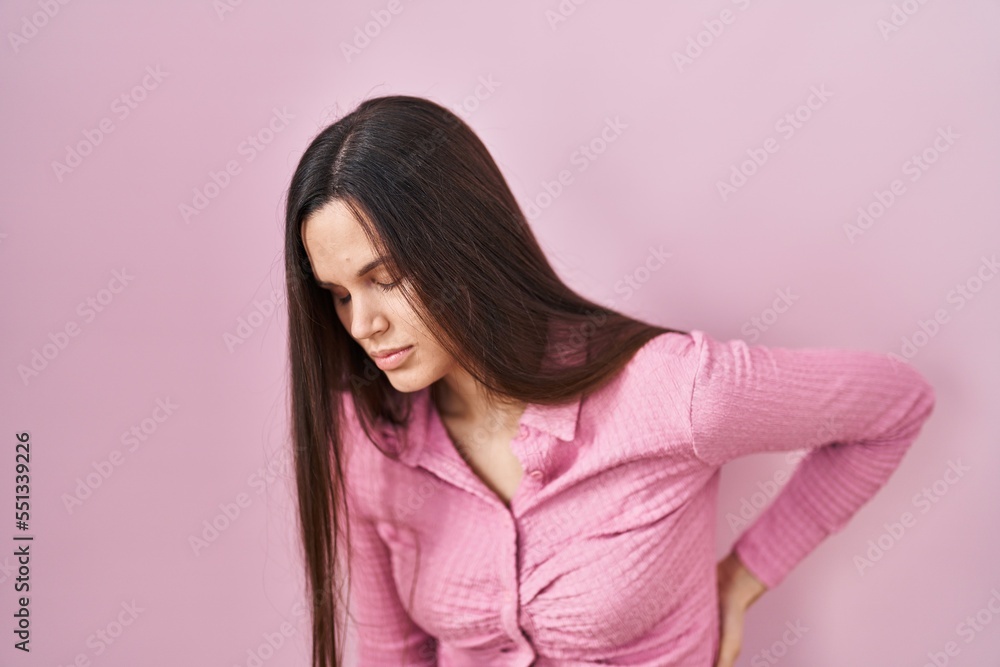 Fototapeta premium Young hispanic woman standing over pink background suffering of backache, touching back with hand, muscular pain