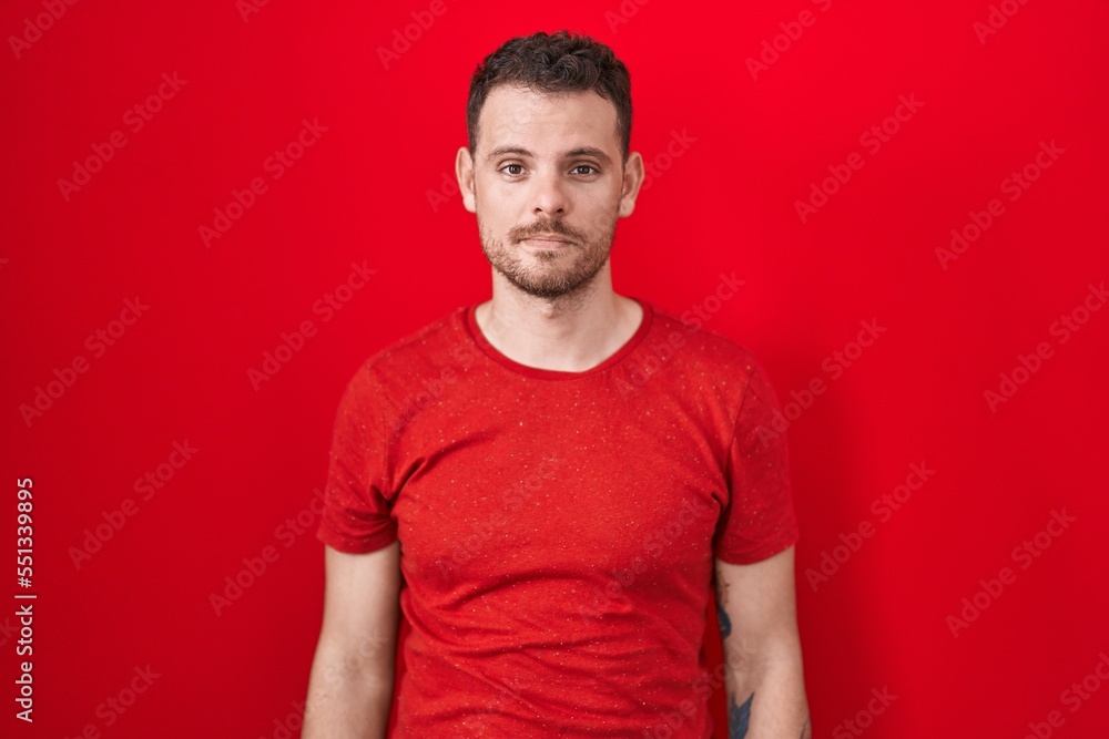 Young hispanic man standing over red background relaxed with serious expression on face. simple and natural looking at the camera. Young hispanic man standing over red background relaxed with serious expression on face. simple and natural looking at the camera.