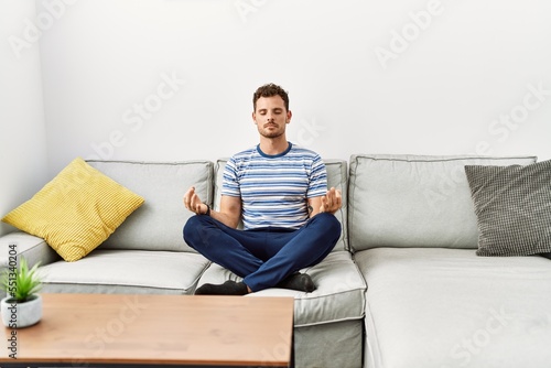 Young hispanic man doing yoga exercise sitting on the sofa at home