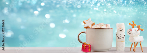 Christmas mug with hot chocolate and marshmallows. XMas handmade marshmallow snowman and christmas deer. christmas festive banner with snowly blue glittering background, copy space for text.