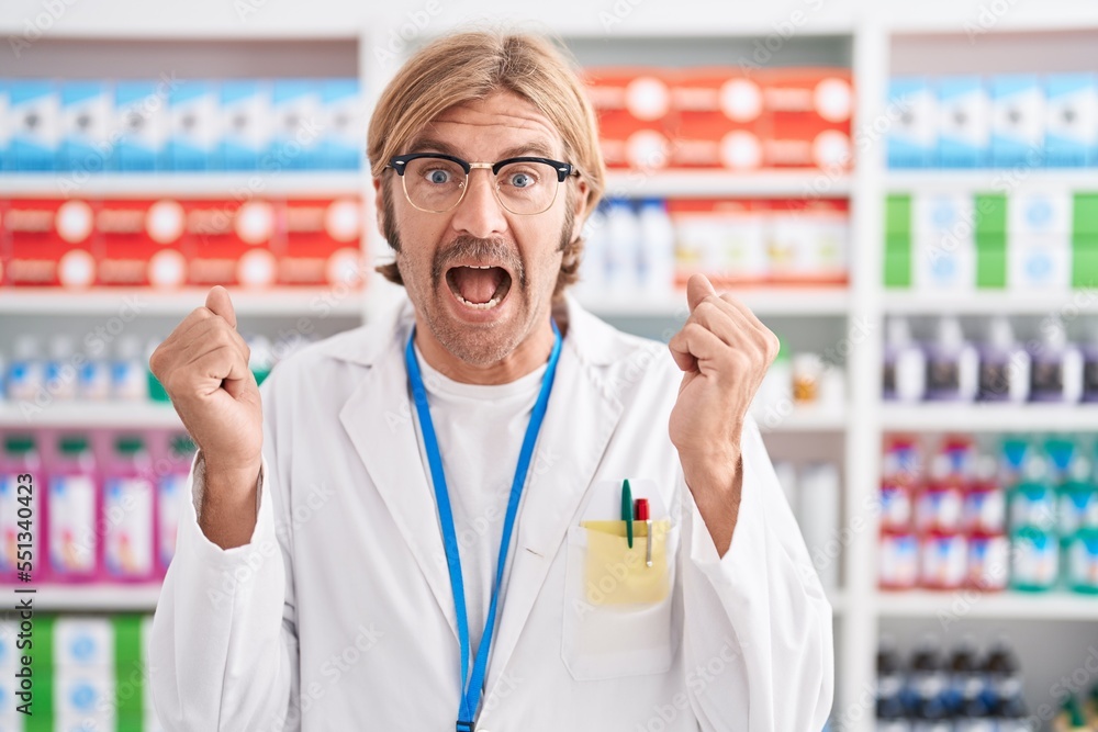 Caucasian man with mustache working at pharmacy drugstore celebrating surprised and amazed for success with arms raised and open eyes. winner concept.