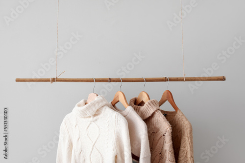 Rack with knitted sweaters hanging on light wall