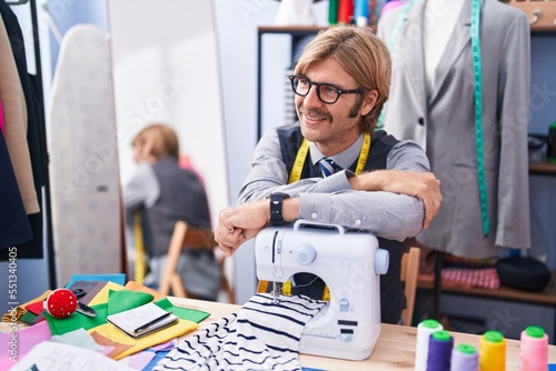 Young blond man tailor smiling confident leaning on sewing machine at clothing factory