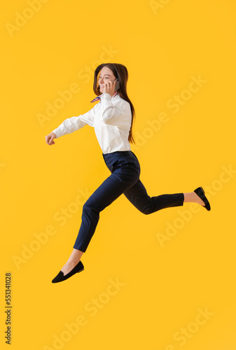 Young assistant talking by mobile phone and jumping on yellow background