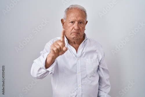 Senior man with grey hair standing over isolated background pointing with finger up and angry expression, showing no gesture