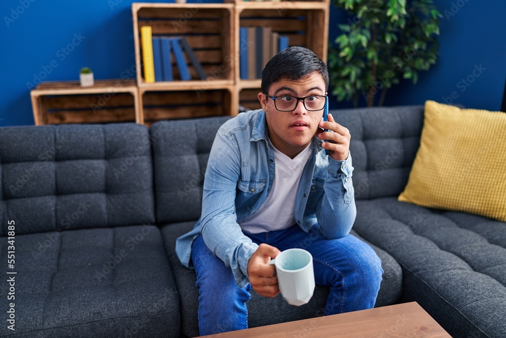 Down syndrome man drinking coffee and talking on the smartphone at home Down syndrome man drinking coffee and talking on the smartphone at home