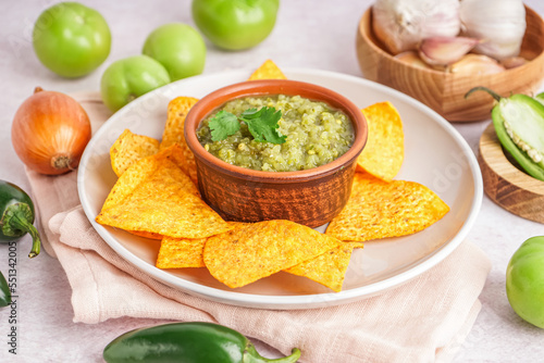 Plate with bowl of tasty green salsa sauce and nachos on light background