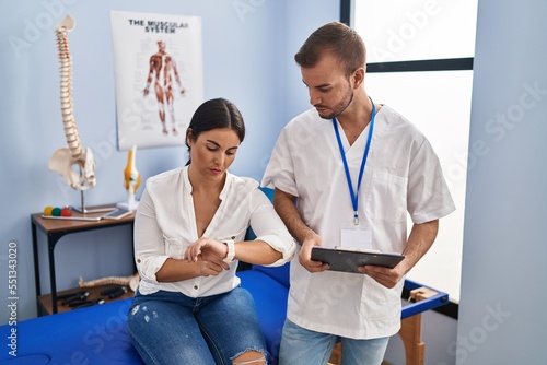 Young hispanic woman at physiotherapist appointment checking the time on wrist watch, relaxed and confident