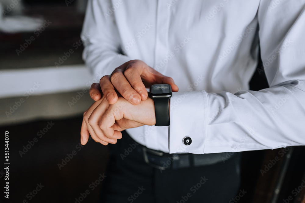 A man, a businessman in a white shirt holds a smartwatch, a wristwatch on his hand, preparing in the morning. Close-up photography, business, portrait. A man, a businessman in a white shirt holds a smartwatch, a wristwatch on his hand, preparing in the morning. Close-up photography, business, portrait.