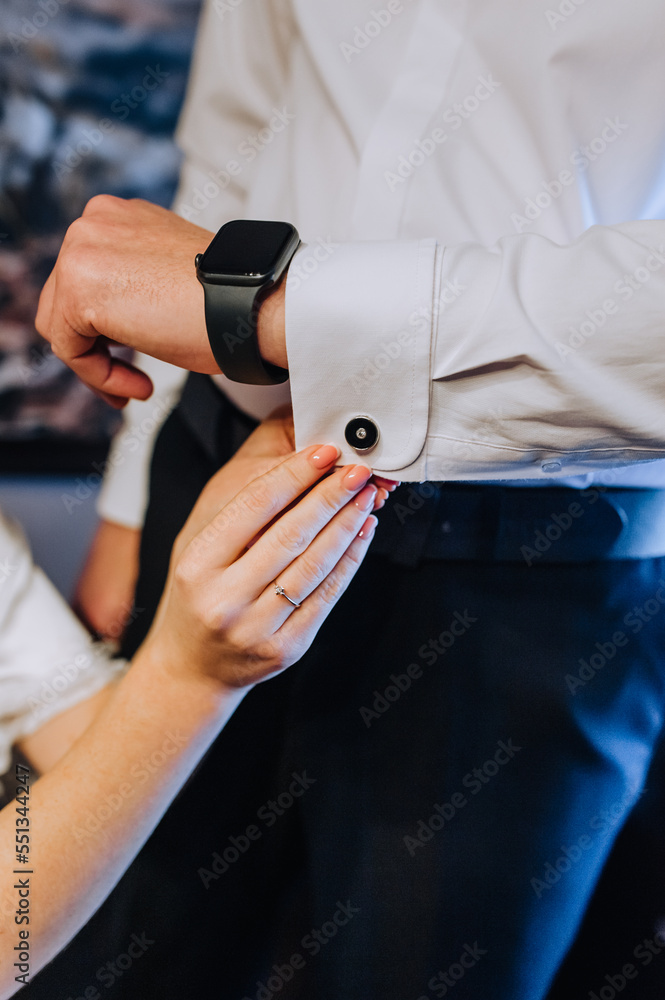 A woman, the bride cares, helps with her hand to fasten the cufflink on the groom's shirt, men with smart watches, wristwatches. Wedding photography, portrait.