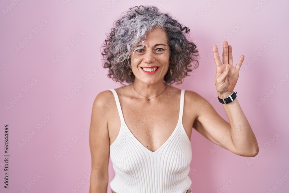 Middle age woman with grey hair standing over pink background showing and pointing up with fingers number four while smiling confident and happy. Middle age woman with grey hair standing over pink background showing and pointing up with fingers number four while smiling confident and happy.