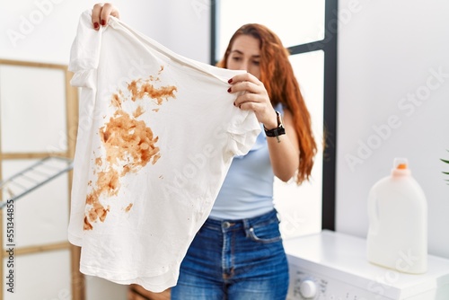 Young redhead woman holding dirty t shirt at laundry room