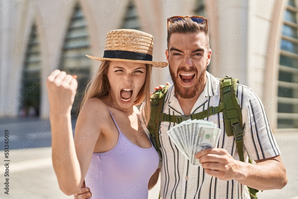 Young tourist couple holding dollars banknotes annoyed and frustrated shouting with anger, yelling crazy with anger and hand raised