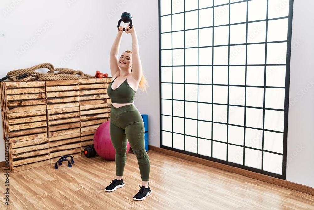 Fototapeta premium Young redhead woman smiling confident training with kettlebell at sport center