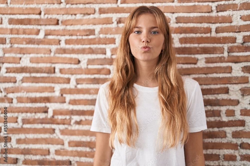 Young caucasian woman standing over bricks wall looking at the camera blowing a kiss on air being lovely and sexy. love expression. Young caucasian woman standing over bricks wall looking at the camera blowing a kiss on air being lovely and sexy. love expression.