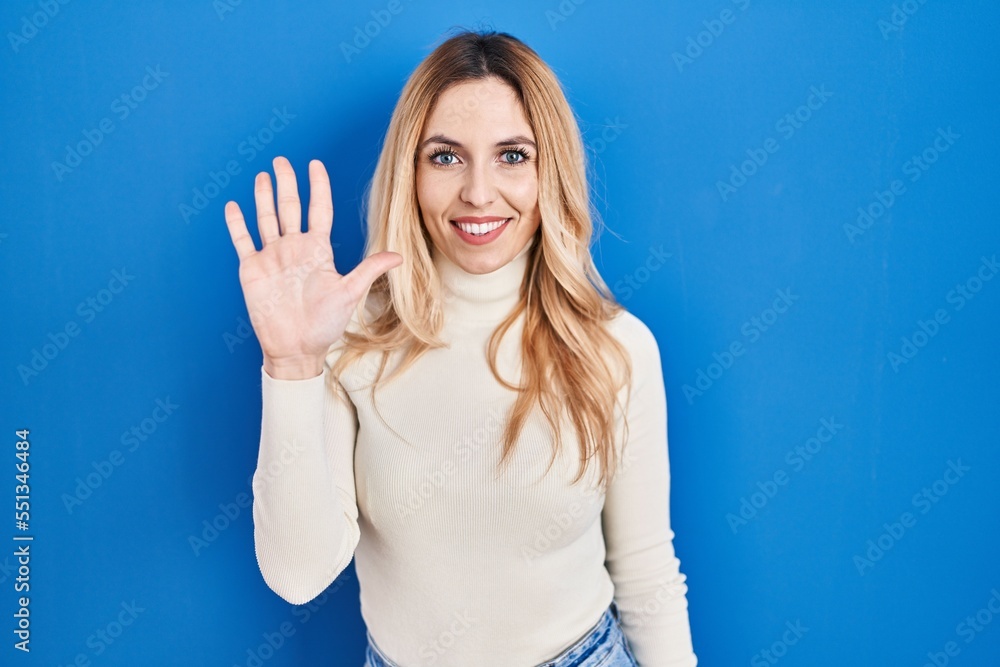 Young caucasian woman standing over blue background showing and pointing up with fingers number five while smiling confident and happy. Young caucasian woman standing over blue background showing and pointing up with fingers number five while smiling confident and happy.