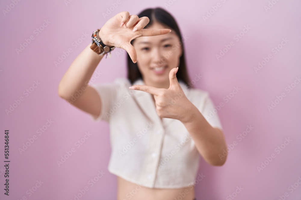 Chinese young woman standing over pink background smiling making frame with hands and fingers with happy face. creativity and photography concept. Chinese young woman standing over pink background smiling making frame with hands and fingers with happy face. creativity and photography concept.