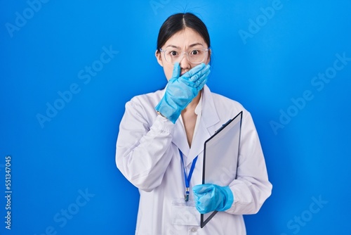Chinese young woman working at scientist laboratory shocked covering mouth with hands for mistake. secret concept.