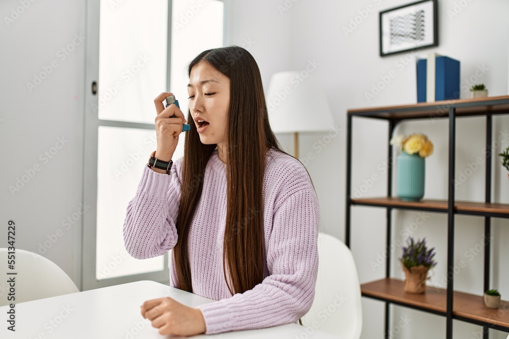 Young chinese girl using inhaler sitting on the table at home. Young chinese girl using inhaler sitting on the table at home.
