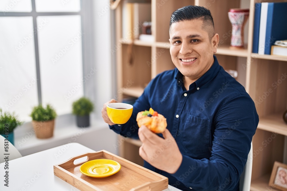 Young latin man having breakfast sitting on table at home Young latin man having breakfast sitting on table at home