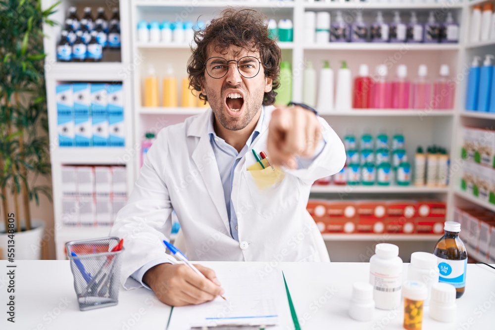 Hispanic young man working at pharmacy drugstore pointing displeased and frustrated to the camera, angry and furious with you