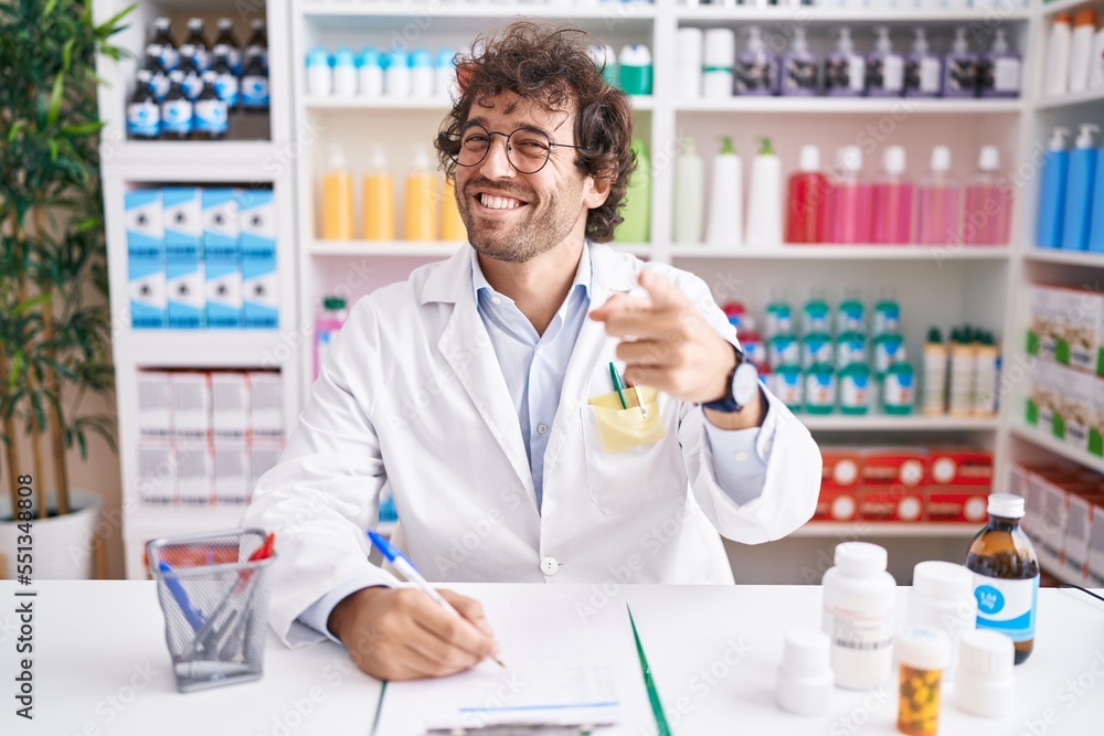 Hispanic young man working at pharmacy drugstore pointing fingers to camera with happy and funny face. good energy and vibes.