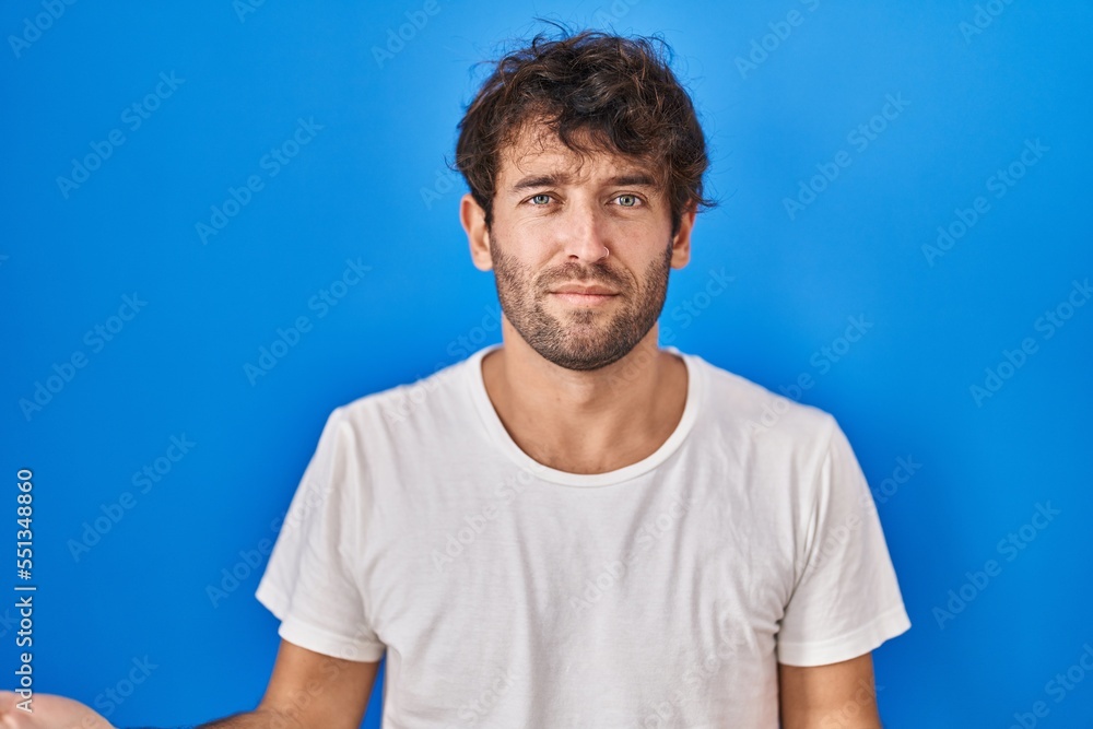 Hispanic young man standing over blue background clueless and confused with open arms, no idea concept. Hispanic young man standing over blue background clueless and confused with open arms, no idea concept.