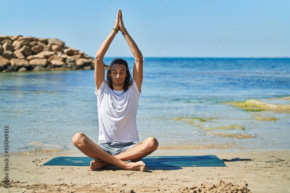 Young hispanic man doing yoga exercise sitting on sand at beach Young hispanic man doing yoga exercise sitting on sand at beach
