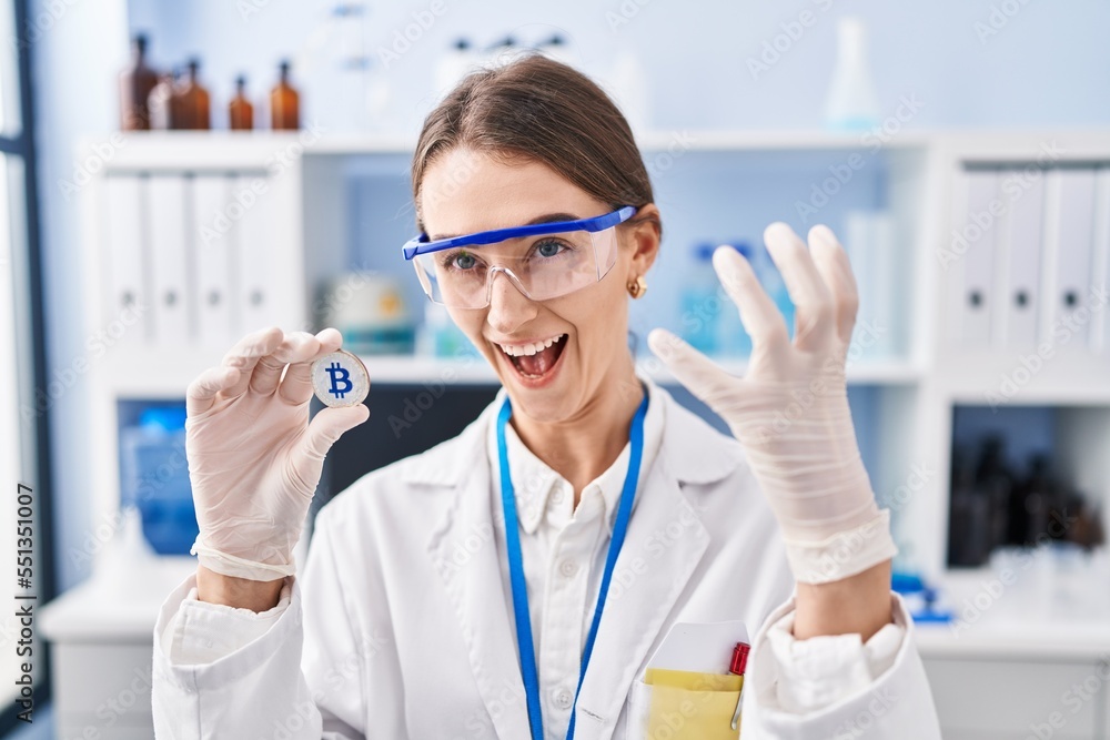 Young caucasian woman working at scientist laboratory holding bitcoin annoyed and frustrated shouting with anger, yelling crazy with anger and hand raised Young caucasian woman working at scientist laboratory holding bitcoin annoyed and frustrated shouting with anger, yelling crazy with anger and hand raised
