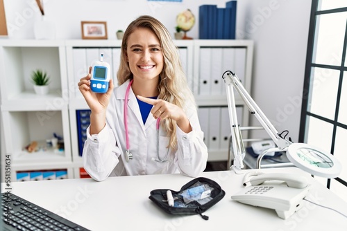 Young beautiful doctor woman holding glucose meter smiling happy pointing with hand and finger