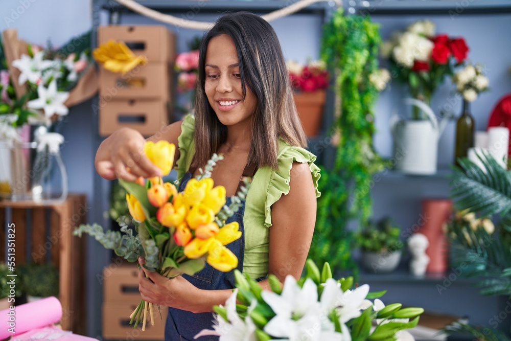 Young hispanic woman florist holding bouquet of flowers at florist store