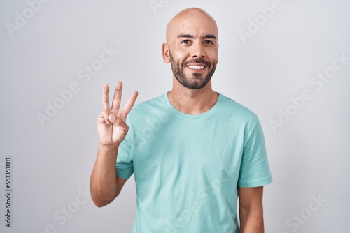Middle age bald man standing over white background showing and pointing up with fingers number three while smiling confident and happy.