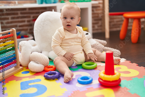 Adorable caucasian baby playing with hoops toy sitting on floor at kindergarten