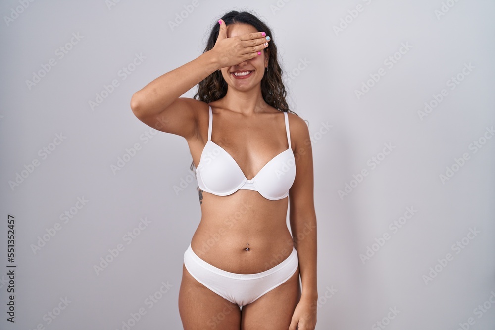 Young hispanic woman wearing white lingerie smiling and laughing with hand on face covering eyes for surprise. blind concept. Young hispanic woman wearing white lingerie smiling and laughing with hand on face covering eyes for surprise. blind concept.