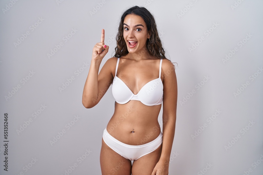 Young hispanic woman wearing white lingerie pointing finger up with successful idea. exited and happy. number one. Young hispanic woman wearing white lingerie pointing finger up with successful idea. exited and happy. number one.