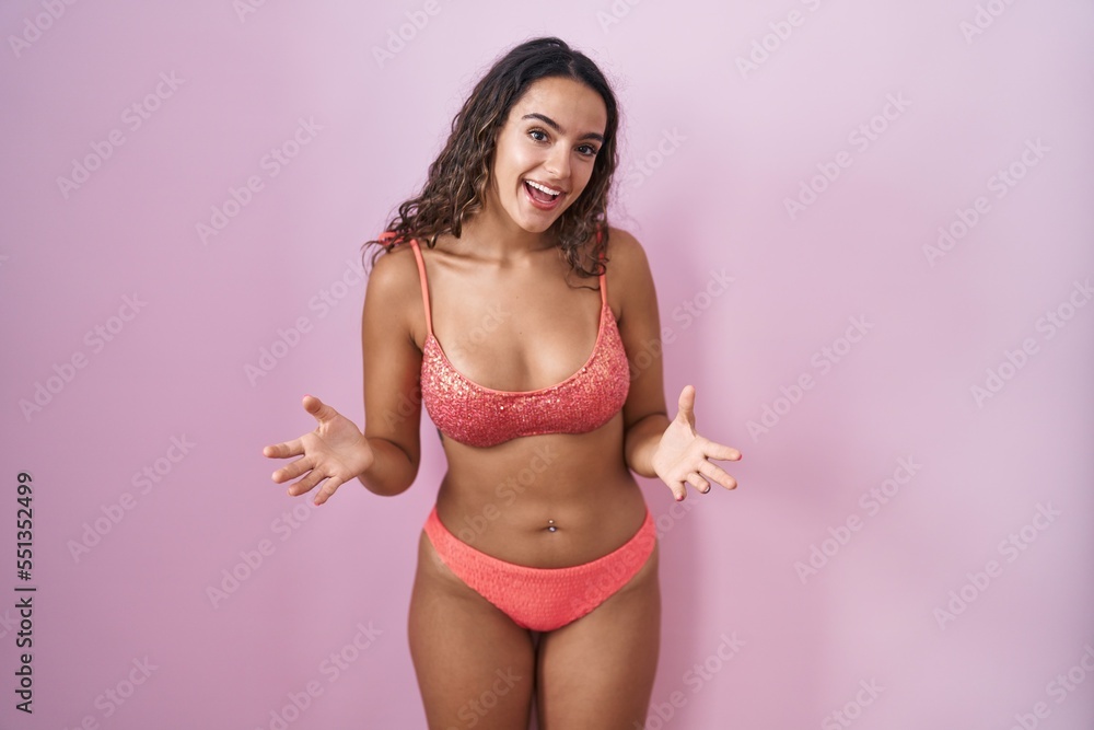 Young hispanic woman wearing lingerie over pink background smiling cheerful with open arms as friendly welcome, positive and confident greetings