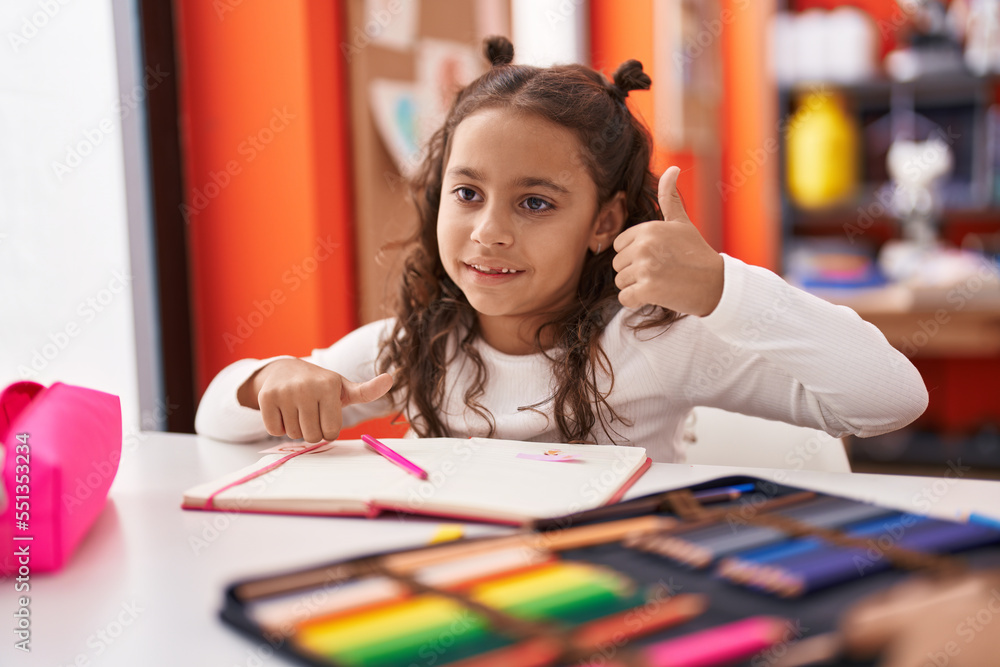 Adorable hispanic girl student sitting on table drawing on notebook at classroom Adorable hispanic girl student sitting on table drawing on notebook at classroom