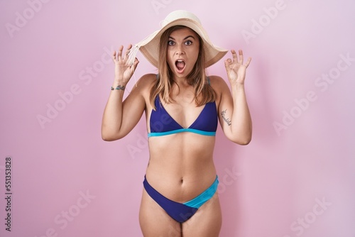Young hispanic woman wearing bikini over pink background looking surprised and shocked doing ok approval symbol with fingers. crazy expression