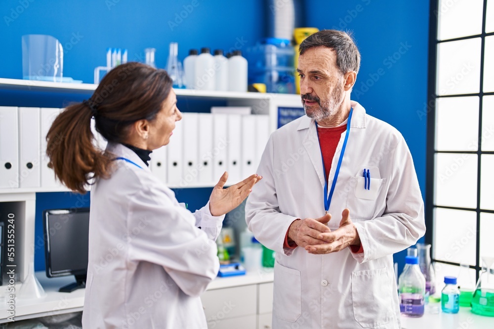 Middle age man and woman scientists having conversation at laboratory Middle age man and woman scientists having conversation at laboratory