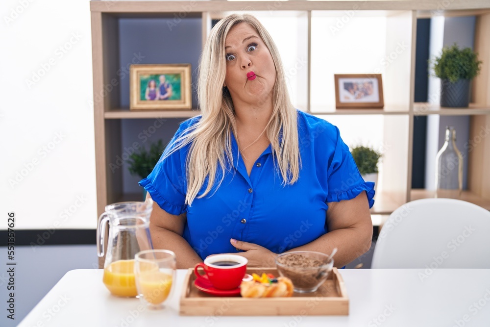 Caucasian plus size woman eating breakfast at home making fish face with lips, crazy and comical gesture. funny expression. Caucasian plus size woman eating breakfast at home making fish face with lips, crazy and comical gesture. funny expression.