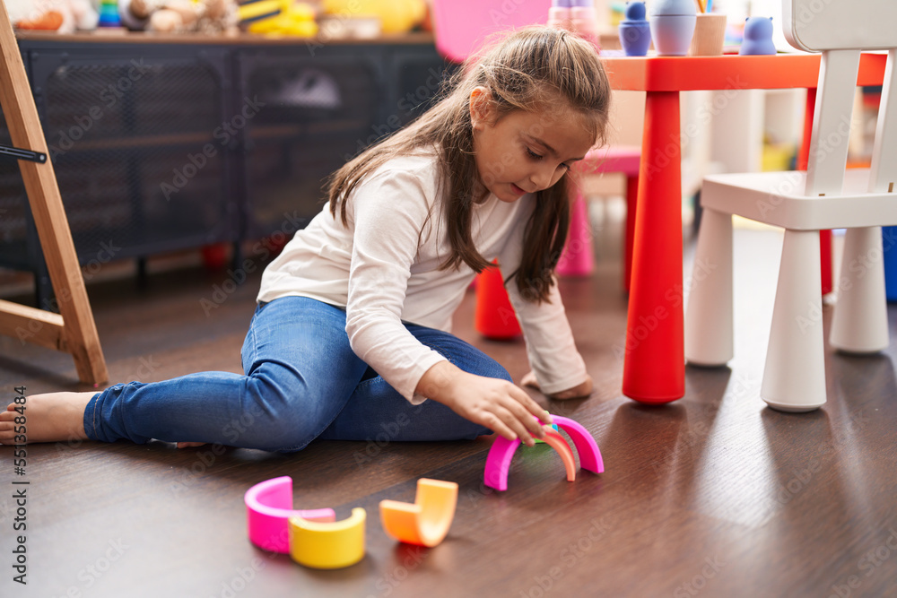 Adorable hispanic girl playing with toys sitting on floor at kindergarten Adorable hispanic girl playing with toys sitting on floor at kindergarten