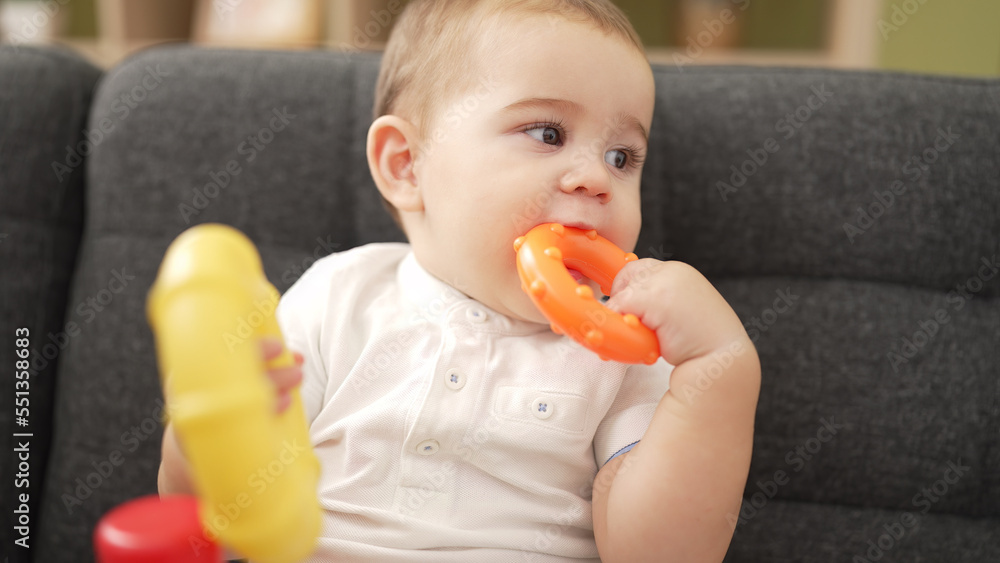 Adorable toddler playing with hoops sitting on sofa bitting hoop at home Adorable toddler playing with hoops sitting on sofa bitting hoop at home