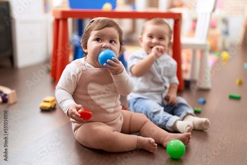 Two toddlers sucking ball sitting on floor at kindergarten