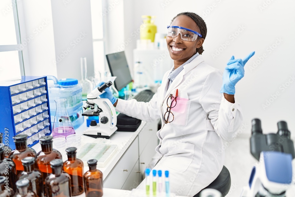 African woman working at scientist laboratory smiling happy pointing with hand and finger to the side African woman working at scientist laboratory smiling happy pointing with hand and finger to the side