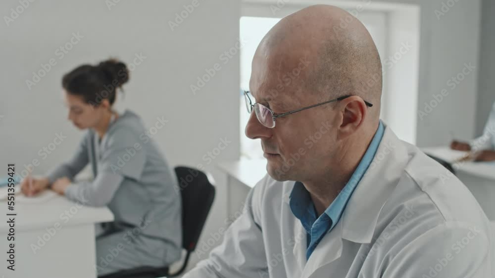 Selective focus medium close-up of mature Caucasian man focused on studying at medical training asking questions to lecturer and making notes Selective focus medium close-up of mature Caucasian man focused on studying at medical training asking questions to lecturer and making notes