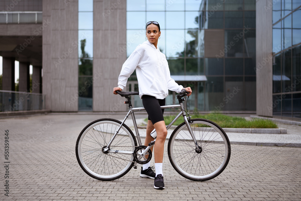 Stylish african american cyclist resting near bicycle on city street 