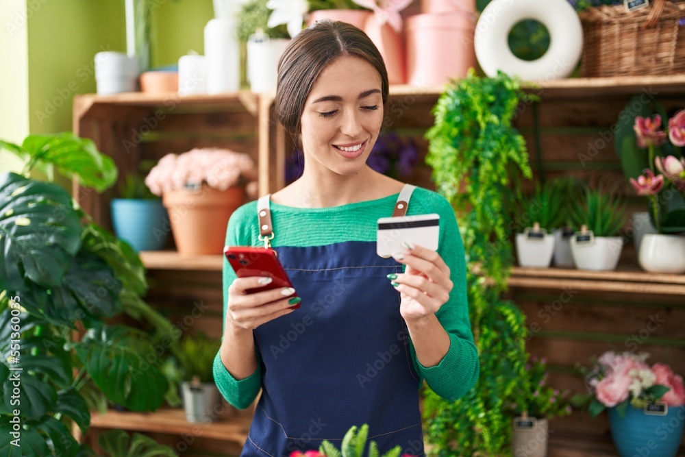 Young beautiful hispanic woman florist using smartphone holding credit card at flower shop Young beautiful hispanic woman florist using smartphone holding credit card at flower shop